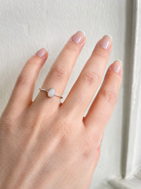 Hand wearing a silver ring with a grey stone on a neutral background