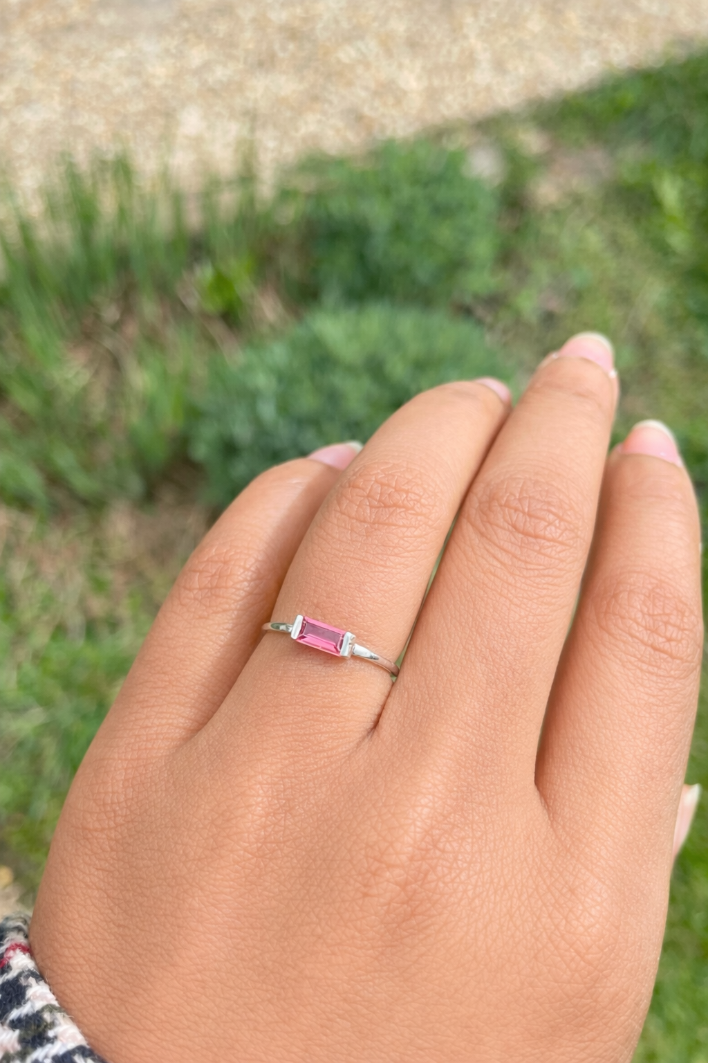 Hand wearing a ring with a Padparadascha gemstone against a blurred green background
