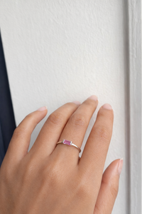 Hand wearing a silver ring with a pink sapphire stone against a white background