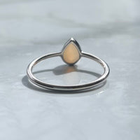 Silver ring with a teardrop-shaped grey stone on a reflective surface