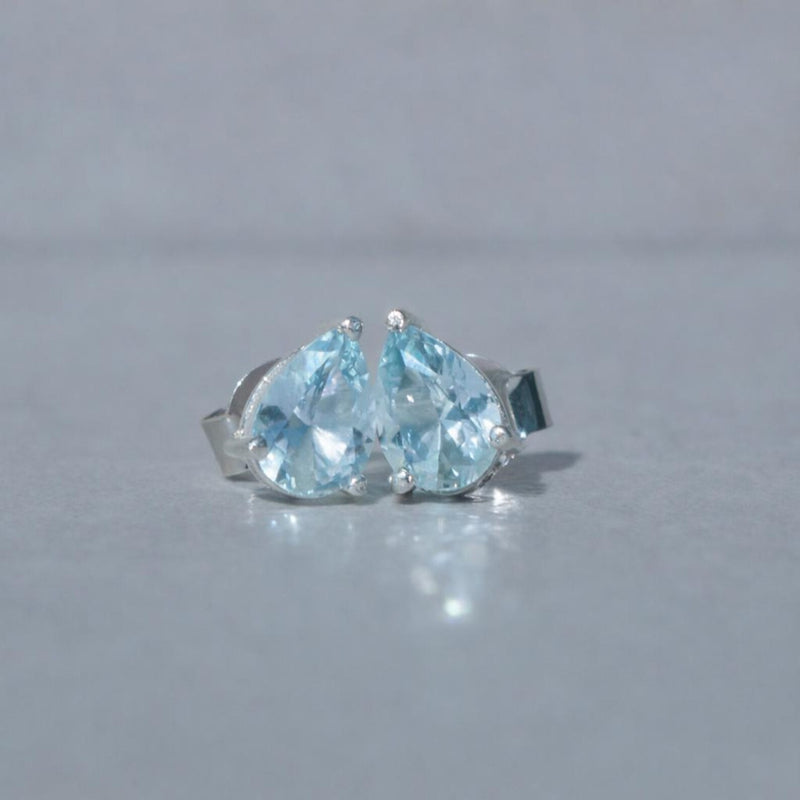 Pair of pear-shaped blue aquamarine gemstones on a silver setting against a gray background