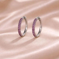 Silver hoop earrings with pink gemstones on a pink satin background