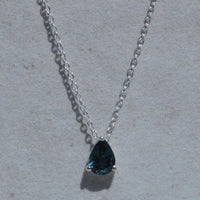 Necklace with a teardrop-shaped blue gemstone on a light gray background