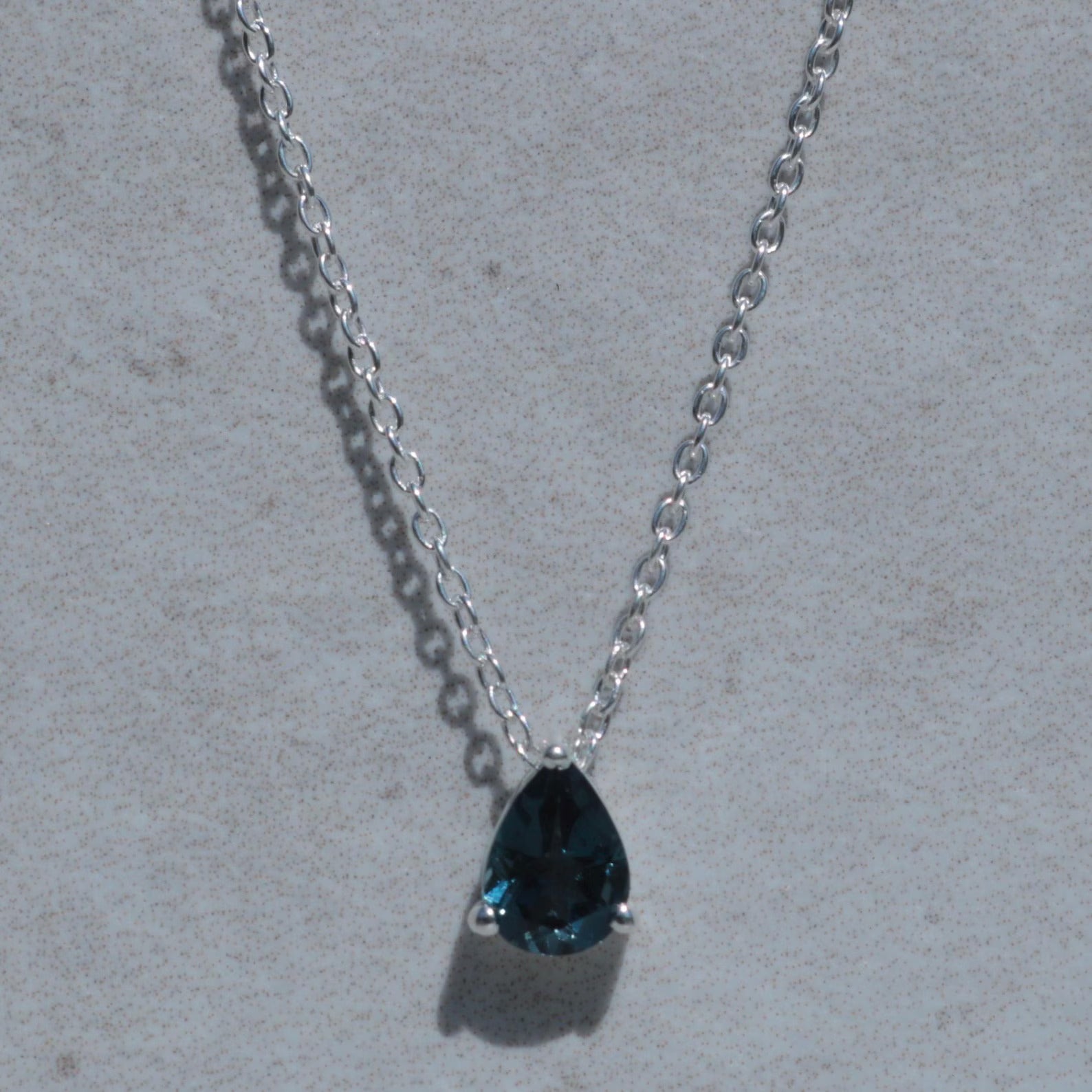 Necklace with a teardrop-shaped blue gemstone on a light gray background