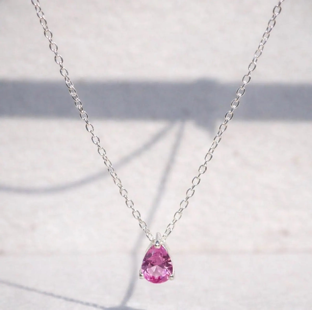 Pink sapphire teardrop pendant on a silver chain against a light background