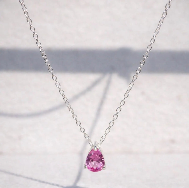 Pink sapphire teardrop pendant on a silver chain against a light background
