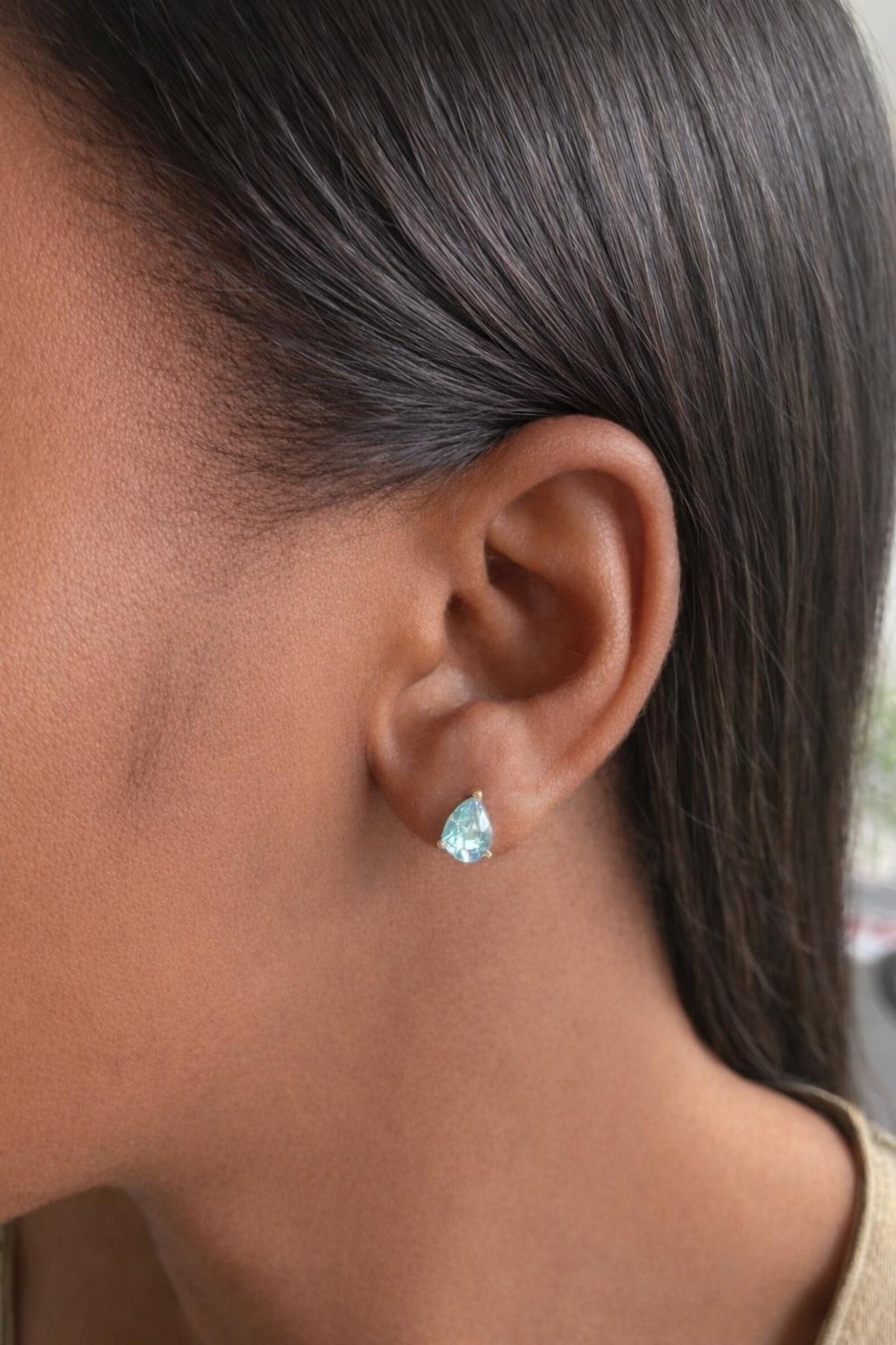 Close-up of an ear wearing a aquamarine teardrop earring with blurred background