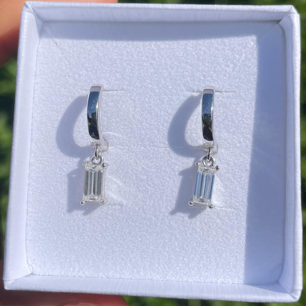 Silver hoop earrings with baguette-cut gemstones in a white jewelry box.