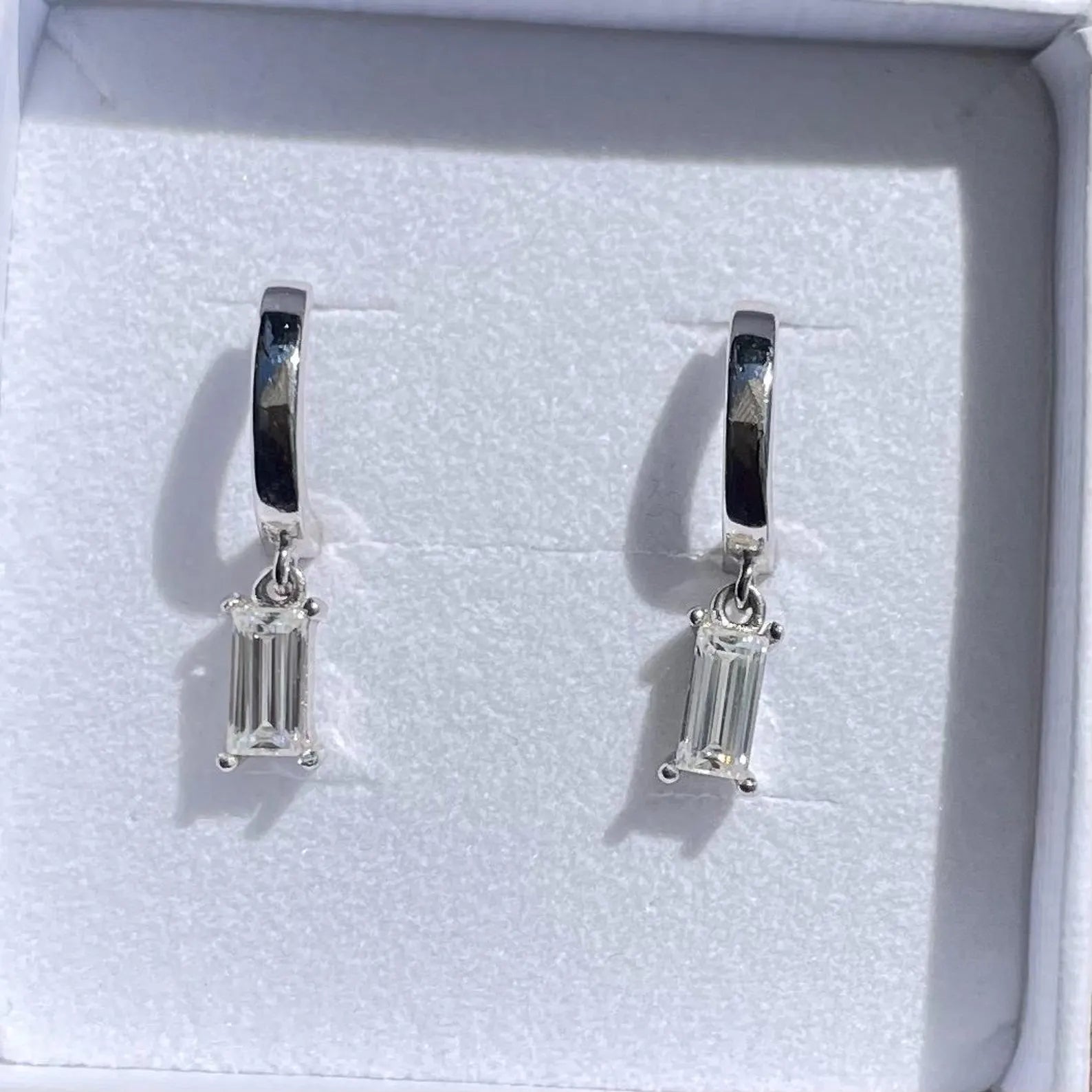 Pair of silver hoop earrings with baguette cut gemstones in a white box.