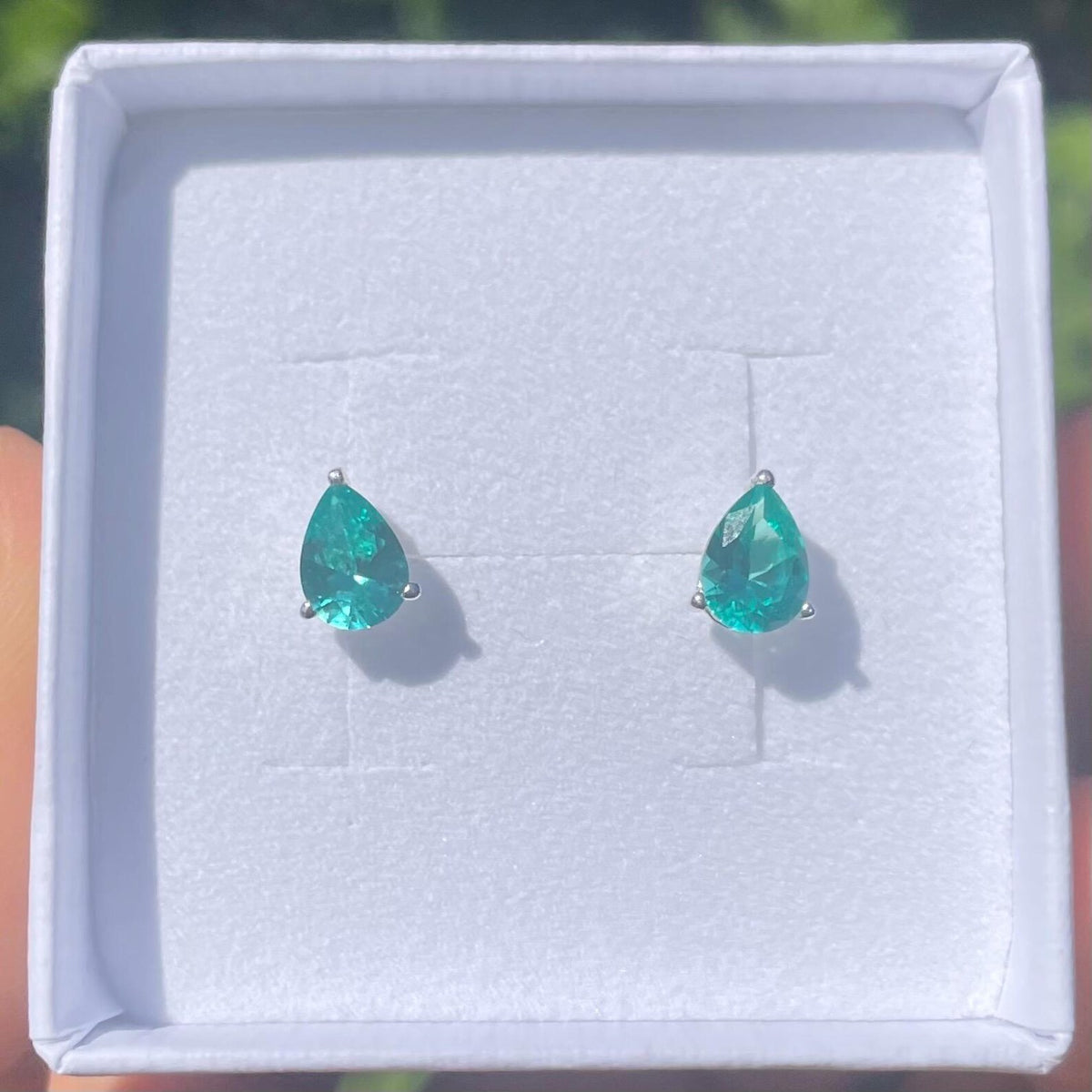 Teardrop-shaped green gemstone earrings in a white jewellry box.