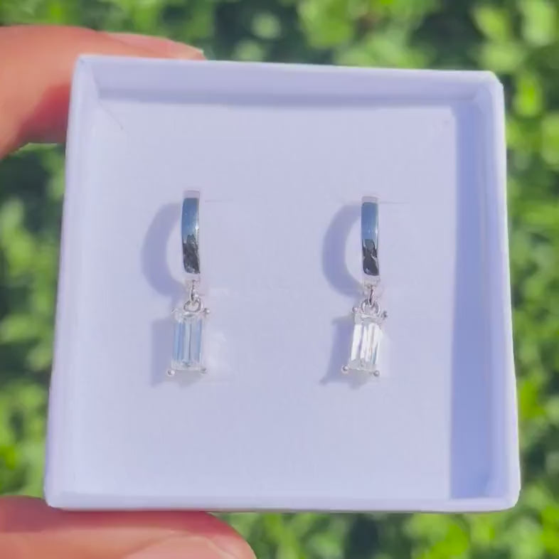 Silver hoop earrings with baguette-cut gemstones in a white jewelry box.